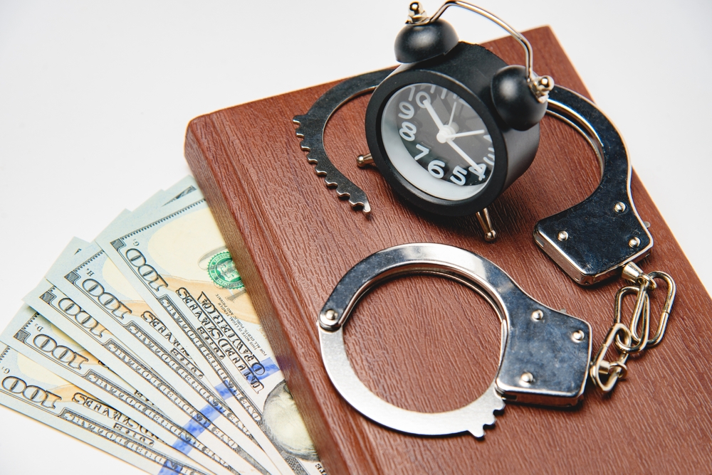 Pack of dollar bills, handcuffs, a book and an alarm clock. Concepts of financial mischief, corruption, swindle and criminality